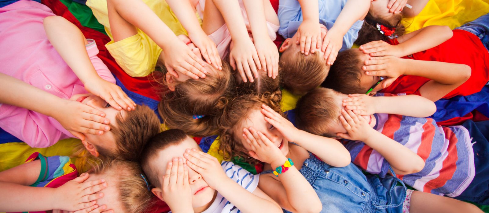 Top view children covering faces by hands, laying on a floor very closely, touching their heads and hair. Kids trying to relax after active games.